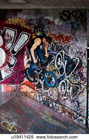 Stock Photography - Youths practicing bike wheelies against graffiti wall backdrop. Fotosearch