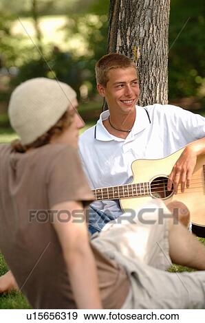 Stock Photo - 2 young guys playing guitar in park, Regina, Saskatchewan. Fotosearch