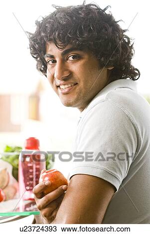 Stock Image - 20 year old man holding organic apple, Brandon, Manitoba, Canada. Fotosearch
