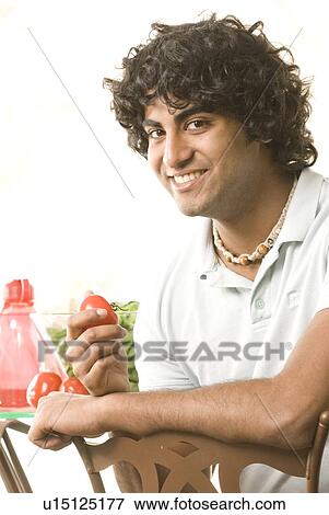 Stock Photo - 20 year old man holding organic tomato, Brandon, Manitoba, Canada. Fotosearch