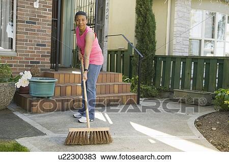 Stock Image - African American woman sweeping her sidewalk, Vancouver, BC. Fotosearch