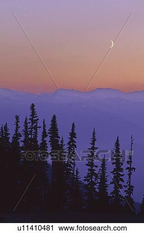 Stock Image - Crescent moon rises in sunset over mountains, Whistler, BC Canada. Fotosearch
