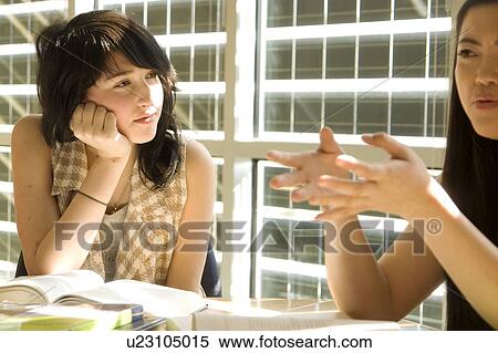 Stock Photography - Female student listens to another student, in front of solar panelled windows, Winnipeg, Canada. Fotosearch