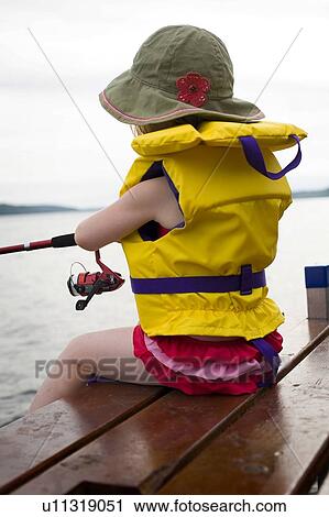 Stock Image - Little girl wearing hat and life preserver fishing off the end of dock, Echo Lake, Saskatchewan, Canada. Fotosearch