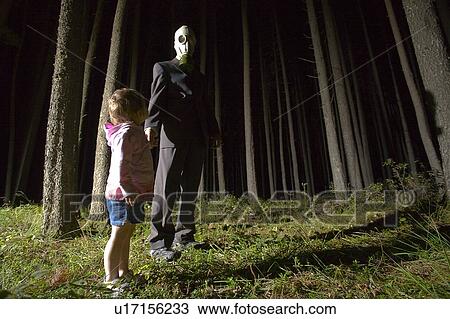 Stock Image - Low angle of Cypress Hills, man in gas mask with little girl in eerie trees at night. Fotosearch