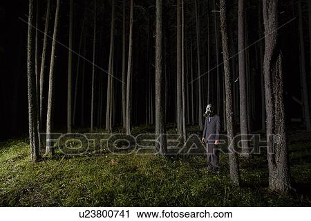 Stock Image - Man in gas mask and suit stands beside eerie trees at night, Cypress Hills, Saskatchewan. Fotosearch