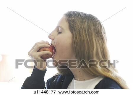 Stock Photo - Pre-teen girl eating organic apple, wearing hoodie made of with hemp fibre, Canada, Manitoba, Brandon. Fotosearch