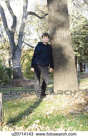 Stock Image - Teen boy leaning on tree, Winnipeg, Canada. Fotosearch