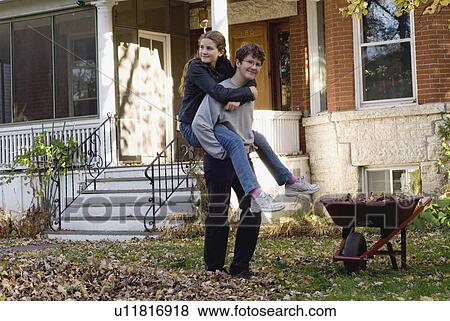 Stock Photo - Teen brother and sister piggyback in autumn leaves, Winnipeg, Canada. Fotosearch