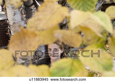 Stock Photography - Teen girl seen through autumn leaves on tree, Winnipeg, Canada. Fotosearch