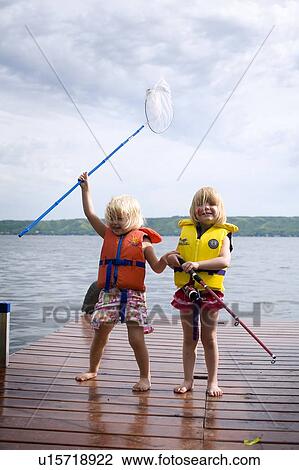 Stock Image - Two young girls wearing life preservers with net and fishing rod on dock, Saskatchewan, Canada. Fotosearch