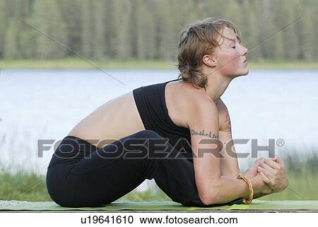 Stock Image - Woman exercising on yoga mat, beside Grayling Lake, Riding Mountain National Park, Manitoba, Canada. Fotosearch