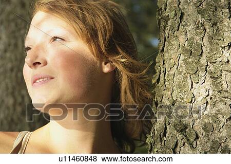Stock Photo - Woman glancing out of frame, beside tree, Riding Mountain National Park, Manitoba, Canada. Fotosearch