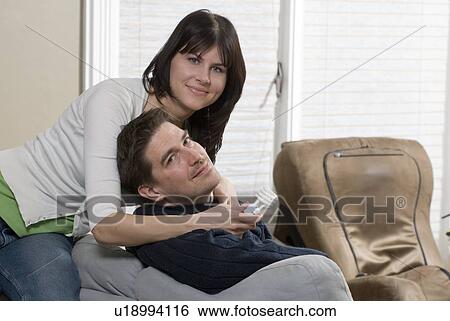 Stock Photograph - Woman holding compact flourescent lightbulb leans over man seated on sofa, Winnipeg, Canada. Fotosearch
