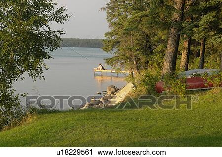 Stock Image - Woman on dock Clear Lake; Canada, Manitoba, Riding Mountain National Park. Fotosearch
