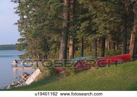 Stock Image - Woman on dock Clear Lake; Canada, Manitoba, Riding Mountain National Park. Fotosearch