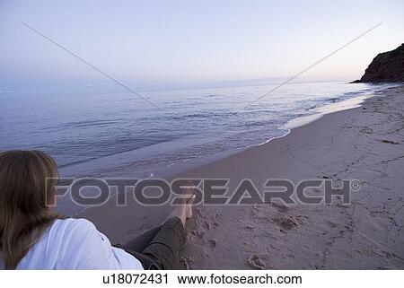 Stock Image - Woman relaxes on beach near Basin Head, Prince Edward Island. Fotosearch