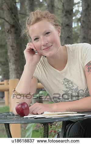 Woman seated at table outdoors, writing, with apple on table, Wasagaming, Riding Mountain National Park, Manitoba, Canada View Large Photo Image Stock Photo - Woman seated at table outdoors, writing, with apple on table, Wasagaming, Riding Mountain National Park, Manitoba, Canada. Fotosearch