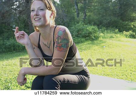 Stock Photo - Woman seated outdoors smokes a cigarette, Grayling Lake, Riding Mountain National Park, Manitoba, Canada. Fotosearch