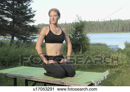 Stock Image - Woman seated upon yoga mat beside lake, Grayling Lake, Riding Mountain National Park, Manitoba, Canada. Fotosearch