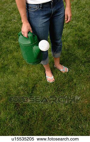 Stock Photography - Woman with watering can from waist down, Regina, Saskatchewan. Fotosearch