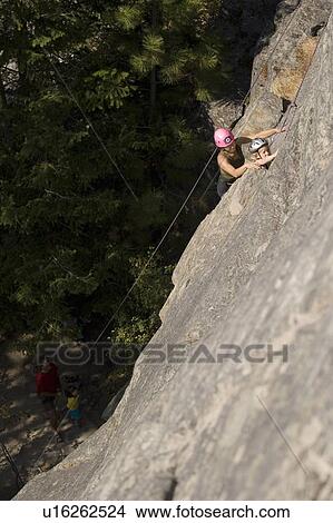 Picture - Young woman climbing with daughter (age 7) up granite cliff while husband/father belays, Stone Hills near Rexford, Montana, USA. Fotosearch