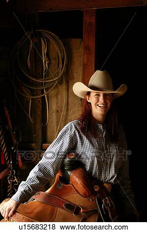 Stock Photo - Young woman holding saddle, Cypress Hills Interprovincial Park, Canada. Fotosearch