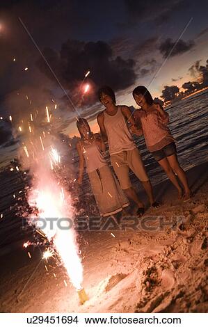 Picture - Three young people looking at lighting firework on beach, long exposure, Saipan, USA . Fotosearch