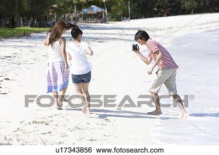 Young man filming women on beach, running, Saipan, USA View Large Photo Image Stock Photograph - Young man filming women on beach, running, Saipan, USA . Fotosearch