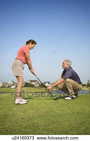 Caucasion mid-adult woman holding golf club while mid-adult man kneels holding club teaching. View Large Photo Image Stock Image - Caucasion mid-adult woman holding golf club while mid-adult man kneels holding club teaching.. Fotosearch
