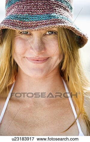 Stock Photo - Close up portrait of smiling attractive young redheaded woman wearing hat and bikini top.. Fotosearch