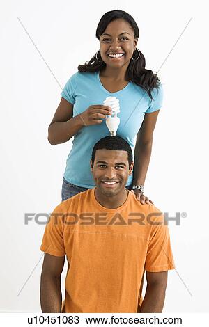 Stock Image - Female holding energy-saving light bulb over man's head. Fotosearch