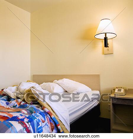 Interior shot of motel room with unmade bed and wall lamp. View Large Photo Image Picture - Interior shot of motel room with unmade bed and wall lamp.. Fotosearch