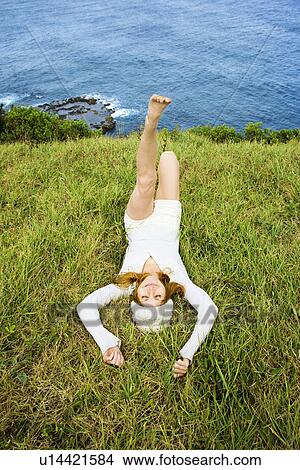 Picture - Joyful young woman relaxing in grass near ocean in Maui, Hawaii.. Fotosearch