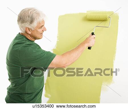 Stock Image - Middle-aged man painting wall green with paint roller.. Fotosearch