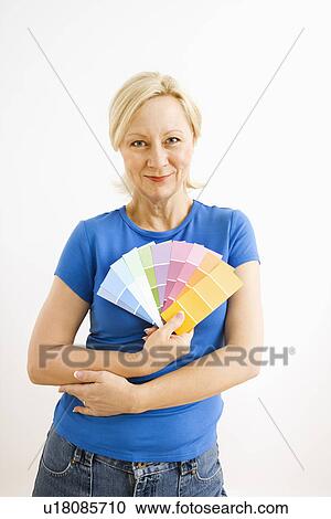 Stock Image - Portrait of smiling adult blonde woman holding paint swatches. Fotosearch