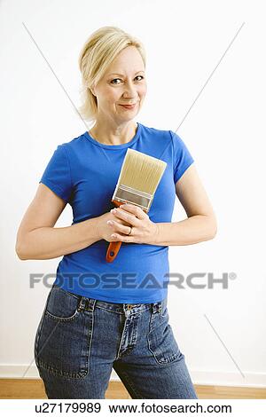 Stock Photo - Portrait of smiling adult blonde woman holding paintbrush.. Fotosearch
