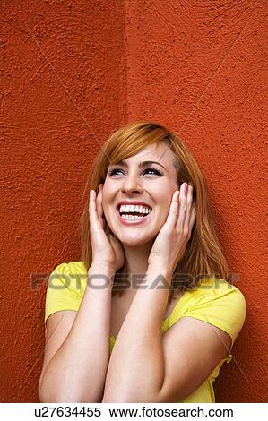 Stock Photography - Smiling young redhead female with hands over ears. Fotosearch