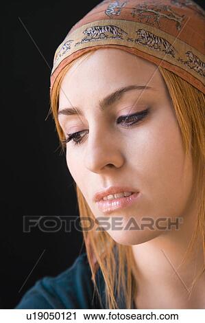 Stock Image - Young redheaded woman wearing cap looking down with serious expression.. Fotosearch