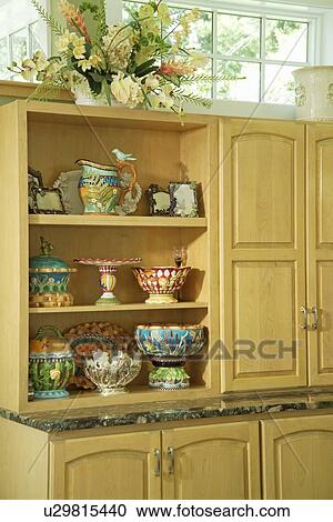 Stock Image - Detail of cabinet with display shelves full of colorful hand painted serving platters and pitchers. Fotosearch