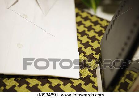 Stock Image - Detail of shirt and iron on ironing board. Fotosearch