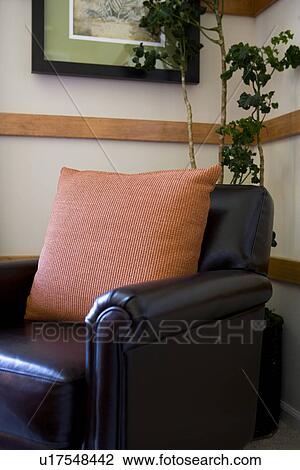 Stock Image - Leather armchair in corner with orange throw pillow. Fotosearch