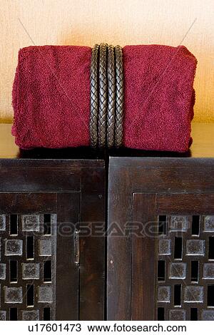 Stock Image - Rolled red towel on top of wooden cabinet. Fotosearch