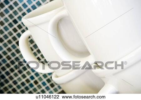 Stock Image - Stacked white coffee mugs in front of tile backsplash. Fotosearch