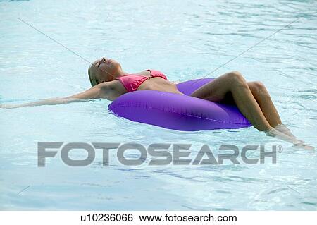Stock Photograph - A young woman floating in a pool. Fotosearch