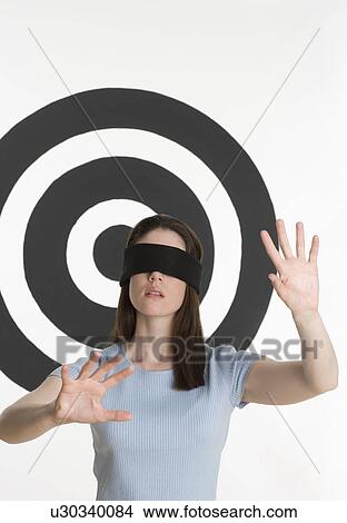 Picture - Blindfolded woman standing in front of bull’s eye. Fotosearch