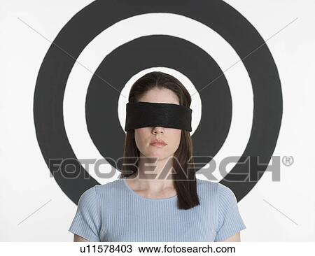 Stock Image - Blindfolded woman standing in front of bull’s eye. Fotosearch