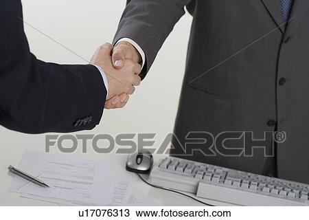 Businessmen shaking hands over computer View Large Photo Image Stock Image - Businessmen shaking hands over computer. Fotosearch