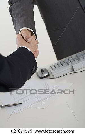 Stock Photo - Businessmen shaking hands over computer. Fotosearch