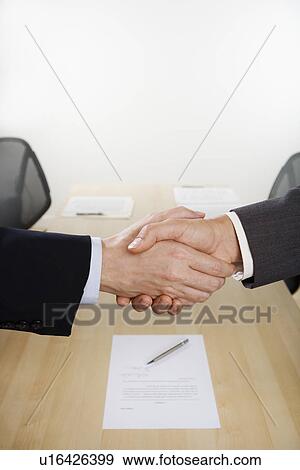 Stock Photo - Businessmen shaking hands over table. Fotosearch